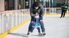 This image shows a father teaching his young child how to skate on the skating rink at Broadway Square.