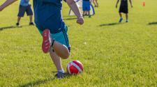 Boy kicking soccer ball in park into 3 boys waiting