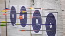 four blue shooting targets hanging on target practice wall with many brightly colored arrows in each target