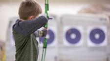 Back of young boy lining up bow and arrow to shoot at target