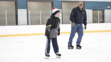 Young boy skating indoors at the Coliseum with an older male skating behind