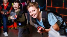 three boys running around playing laser tag with laser tag guns and vests