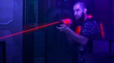 Man walking through dark laser tag background shooting a red laser gun and wearing a vest