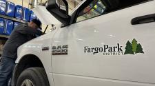 Man is in a shop looking into the engine bay of a white pickup with a Fargo Park District logo on the door of the pickup