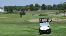 two men waving from a golf cart on a golf course