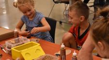 Young girl and boy smiling doing crafts at a table. 