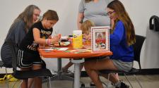 Three young children and their moms sitting at a table working on a craft project. 