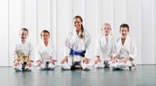 4 kids in Jiu Jitsu robes with an instructor in her robe in front of a white wall
