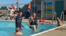 Two male lifeguards in the Madison Pool with three kids taking swimming lessons. The two guys are giving the kids high fives in the water