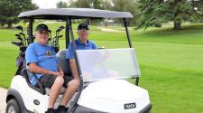 Two older men sit in a golf cart on a golf course during the North Dakota Senior Games.