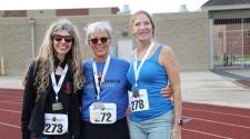 This image shows three women wearing medals smile together on a track after competing in the North Dakota Senior Games.