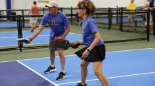 This image shows two senior athletes playing pickleball on an indoor court during the North Dakota Senior Games.