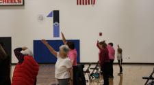 adults 55+ standing in gym with chair next to each stretching for the SAIL program