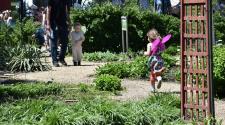 A gravel path winds through a lush garden, providing a walking route between planted garden beds as children and families explore the area.